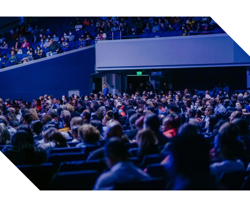 Attendees seated in a conference session listening to a speaker presenting on stage, representing professional conferences, knowledge sharing, networking, and event management services.